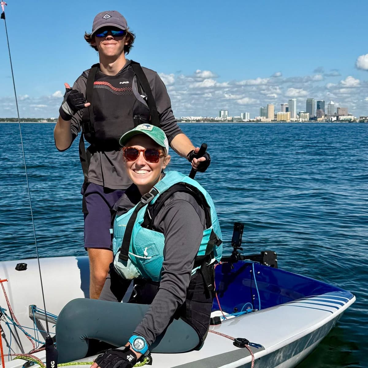 Two teen sailors on a boat with city skyline behind