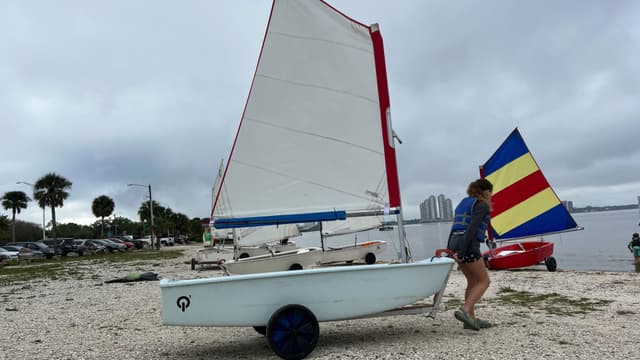 Girl pushing an Optimist sailboat on the beach